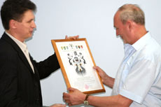 Заместитель председателя Сибирской Геральдической Коллегии А.В.Кошелев вручает герб В.Г.Миллеру